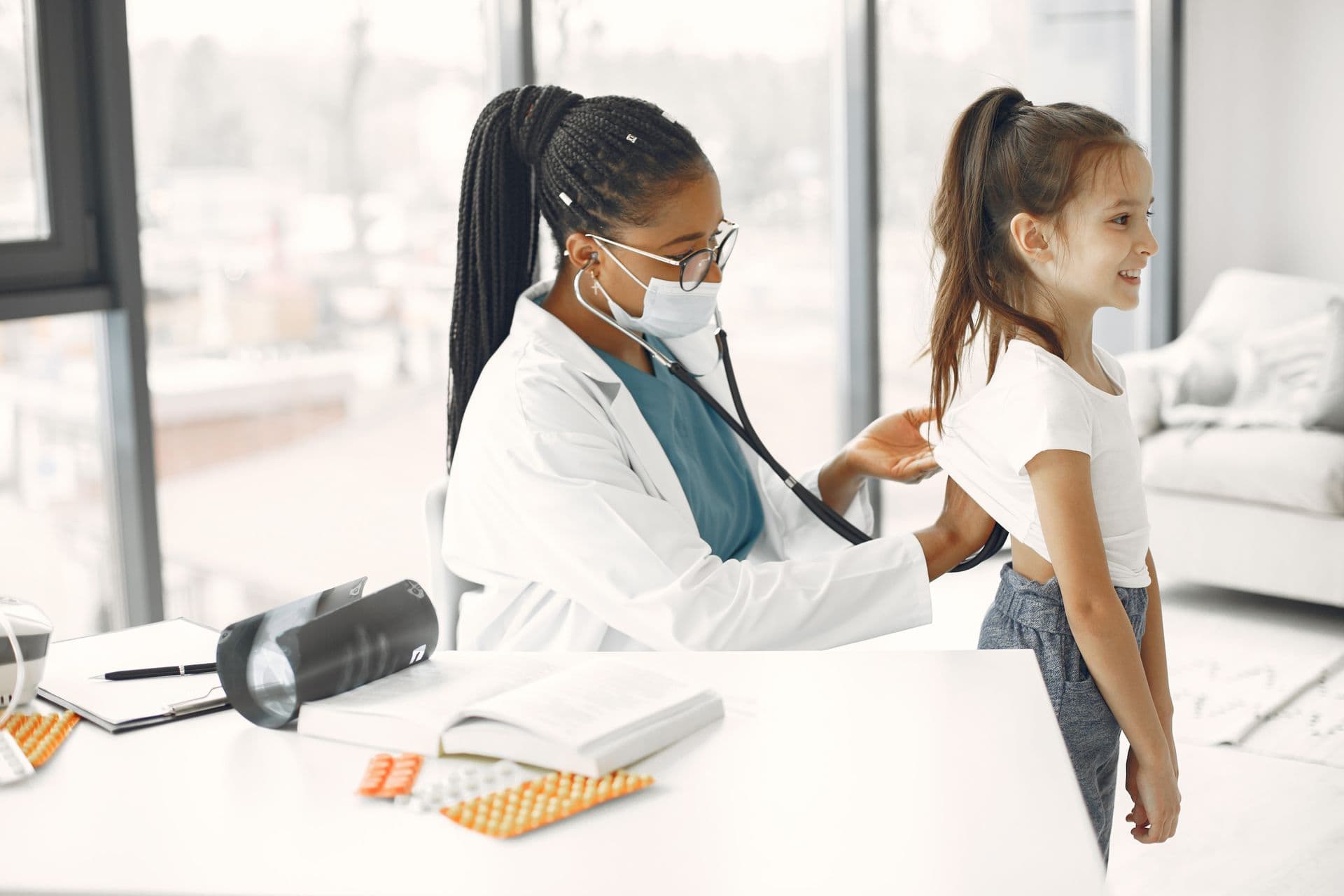A doctor listening to a young patient's back with a stethoscope